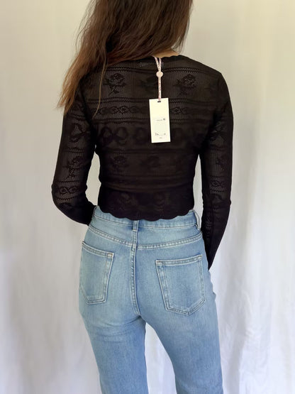Person wearing a black lace top and blue jeans with a white background